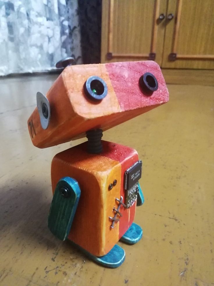 an orange and red toy robot sitting on top of a wooden floor next to a window