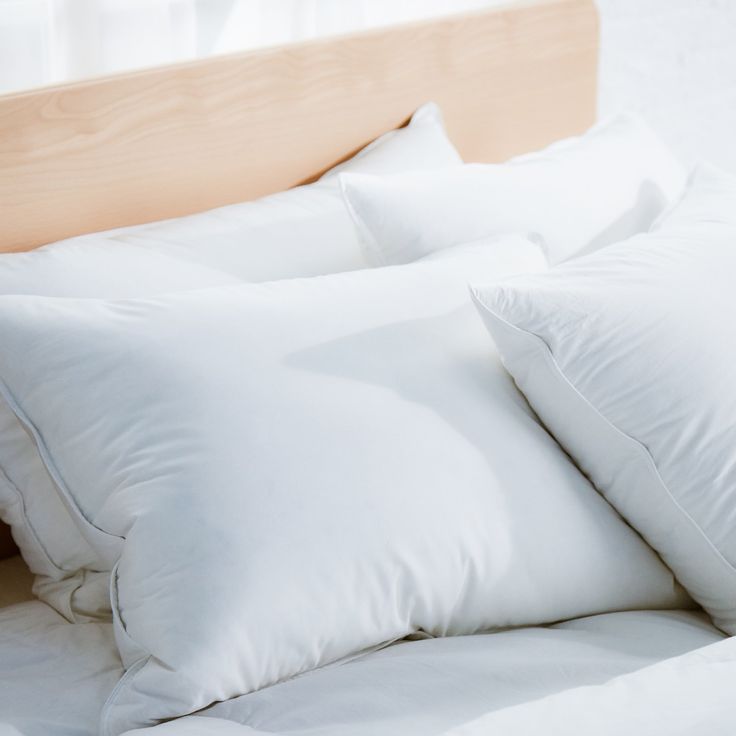 white pillows on a bed with a wooden headboard in the back ground and window behind them