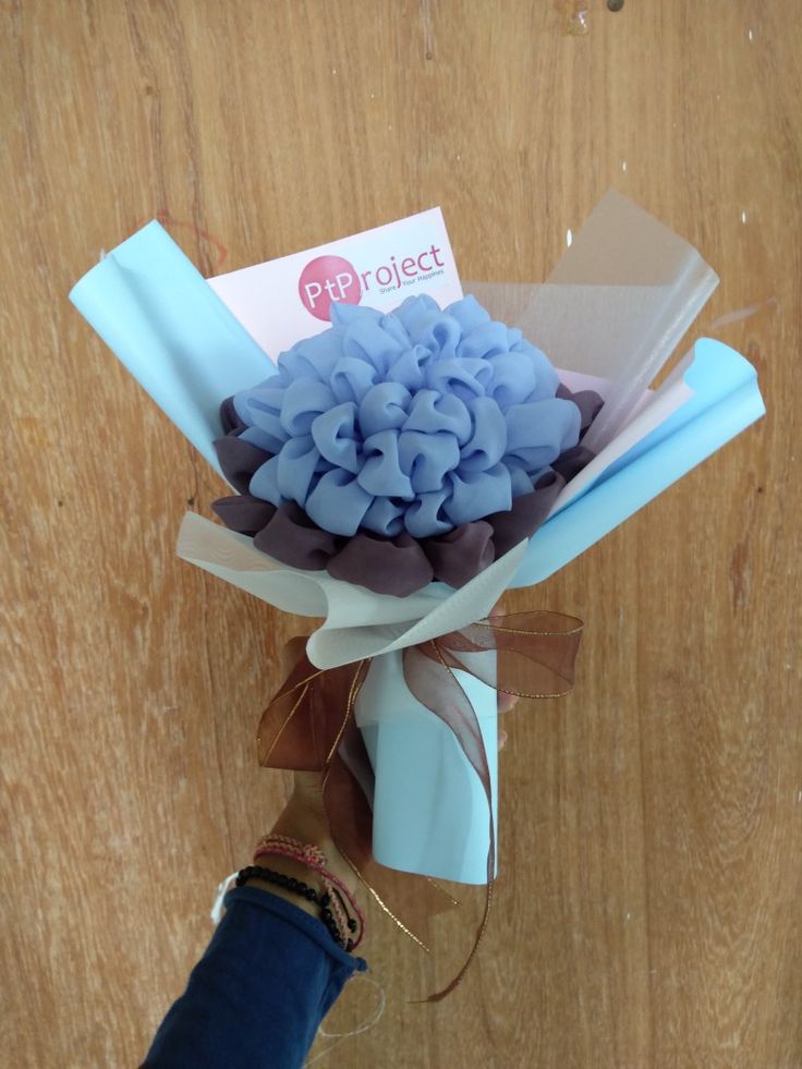 a bouquet of blue and brown flowers is held by someone's hand on a wooden surface