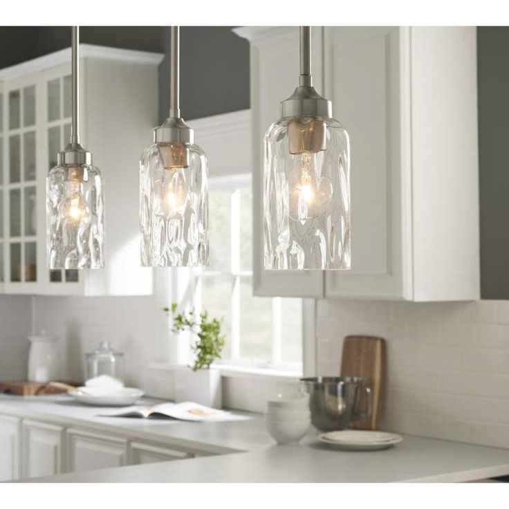 three lights hanging over a kitchen counter in front of a sink and cabinets with white cupboards