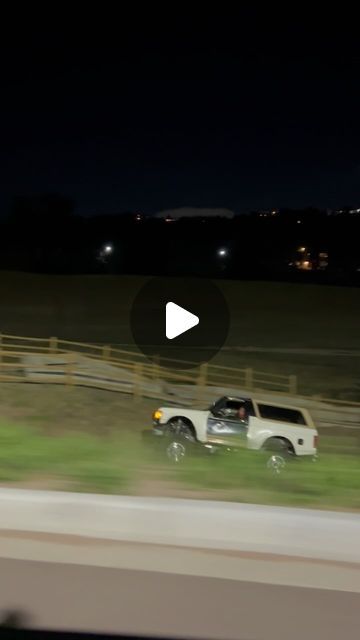 a white truck driving down a road next to a lush green field at night time