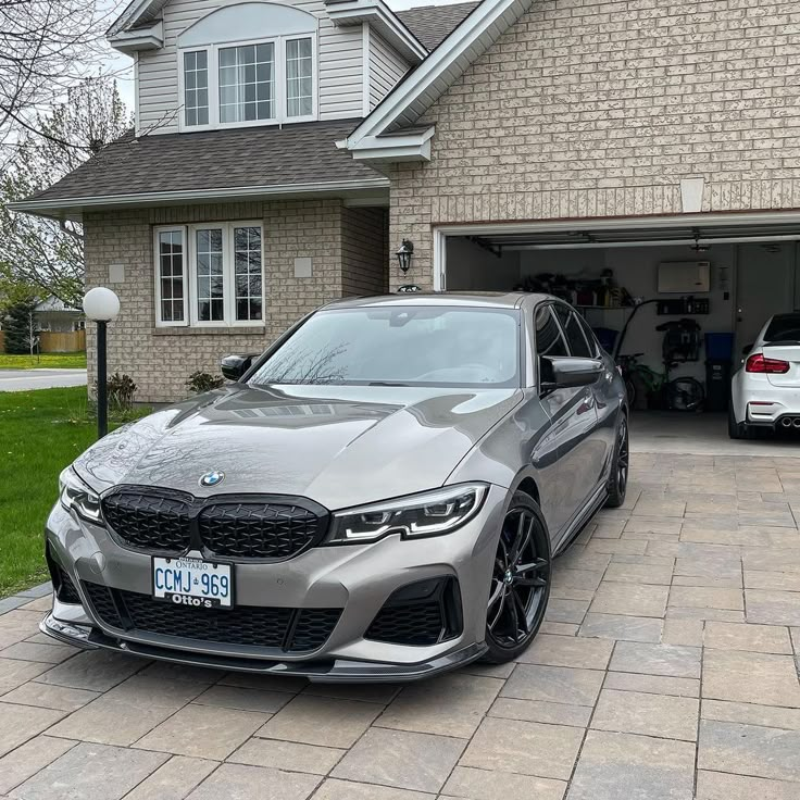 a grey car parked in front of a house next to a white car on the driveway