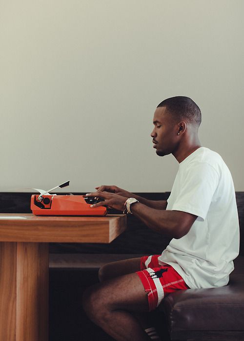 a man sitting at a desk typing on a red typewriter in front of him