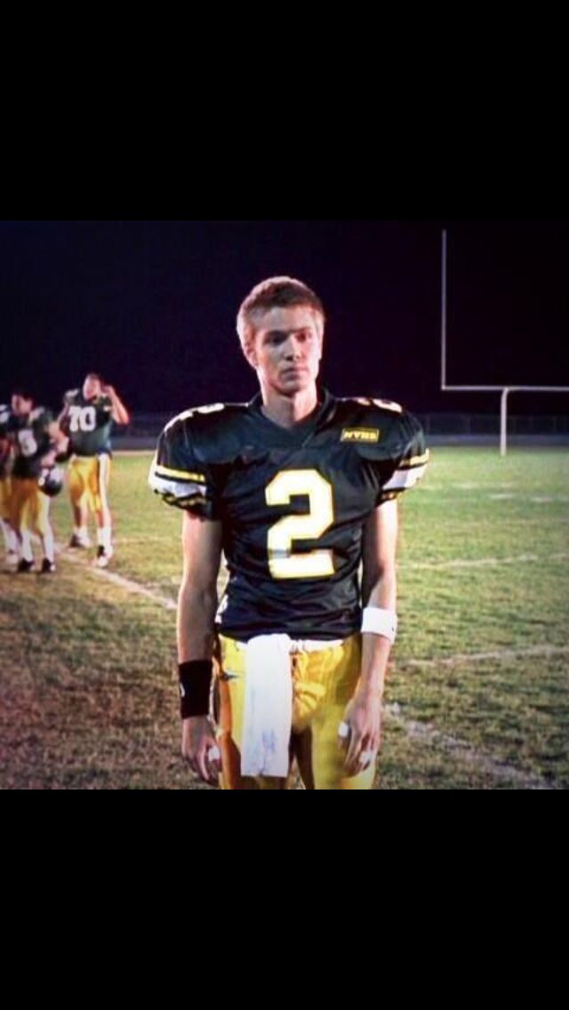 a football player standing on the sidelines with his hands behind his back and other players in the background