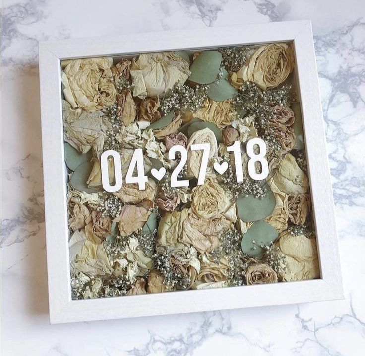 a white box filled with dried flowers on top of a marble counter next to a clock