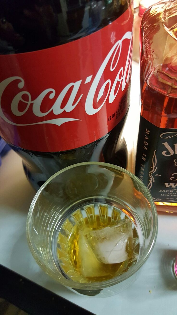 a bottle of coca cola next to a glass with ice cubes