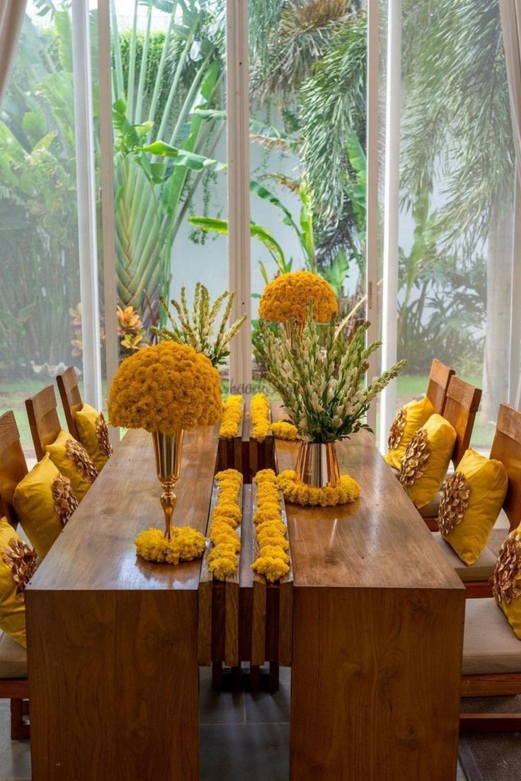 a wooden table topped with lots of yellow flowers next to a window covered in curtains