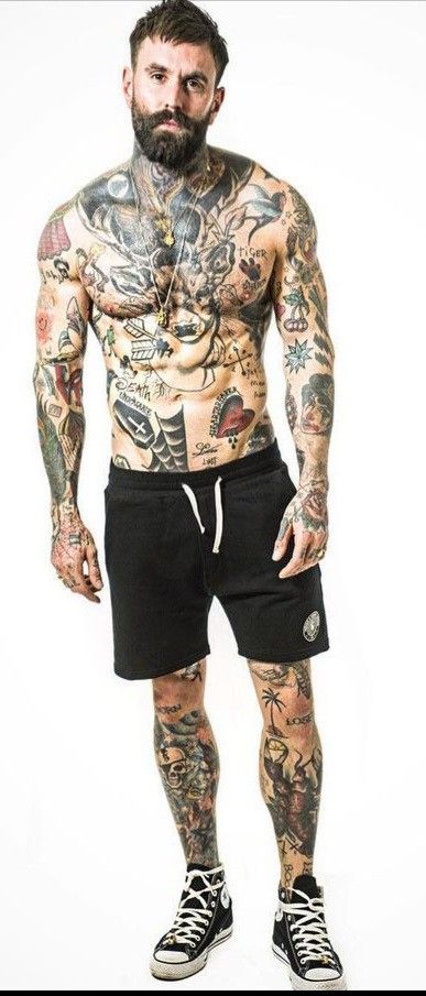 a man with tattoos and no shirt on standing in front of a white background wearing black shorts