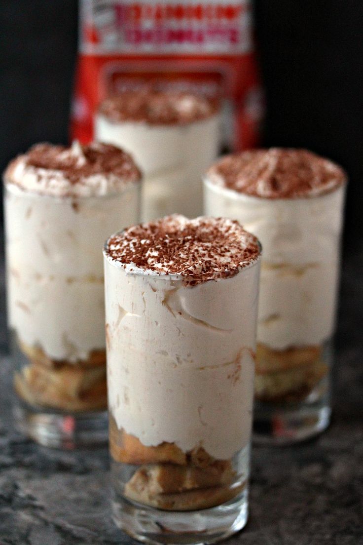 three desserts are sitting in small glasses on a table with a bottle behind them