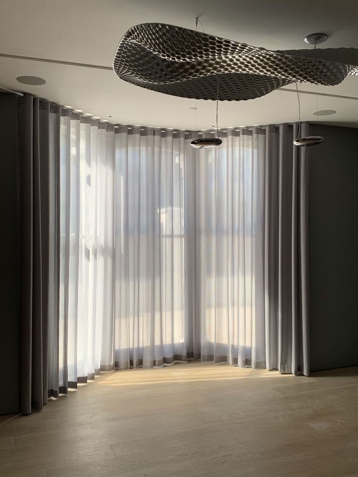 an empty room with sheer curtains and large windows