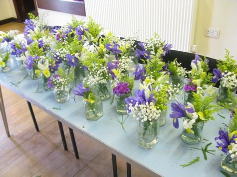 there are many vases with flowers in them on the long table, all lined up and ready to be placed