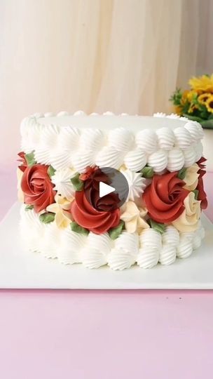 a white cake with red and yellow flowers on the top is sitting on a pink table