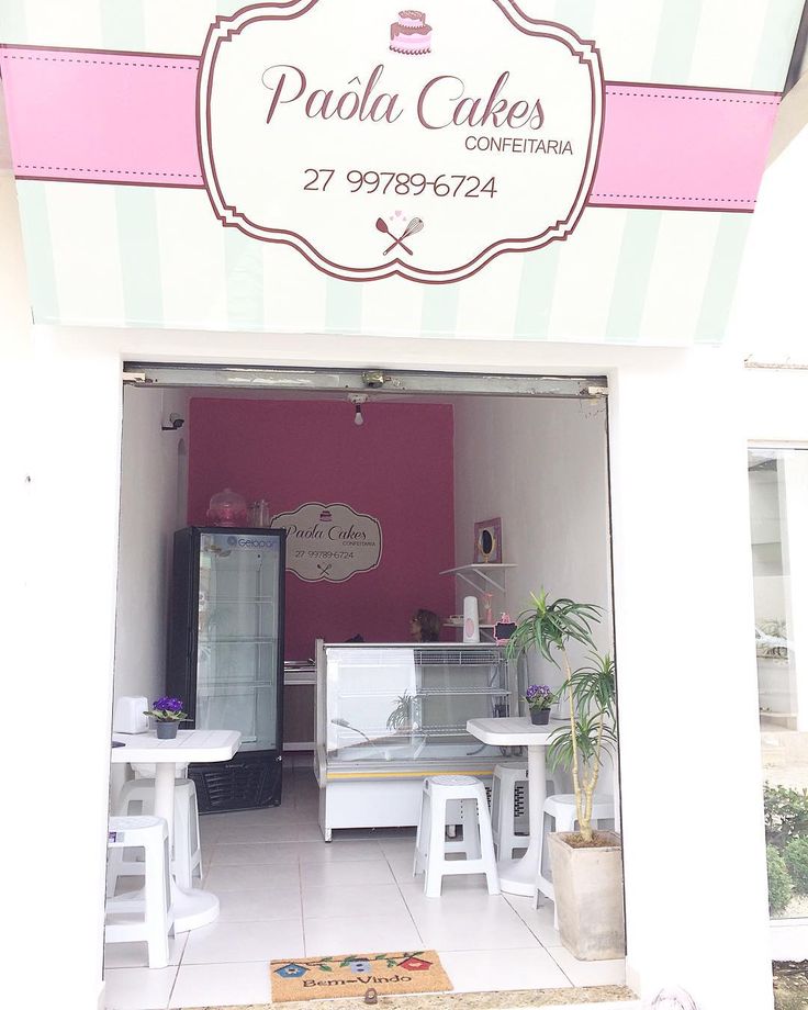 the inside of a cake shop with pink walls and white tables in front of it