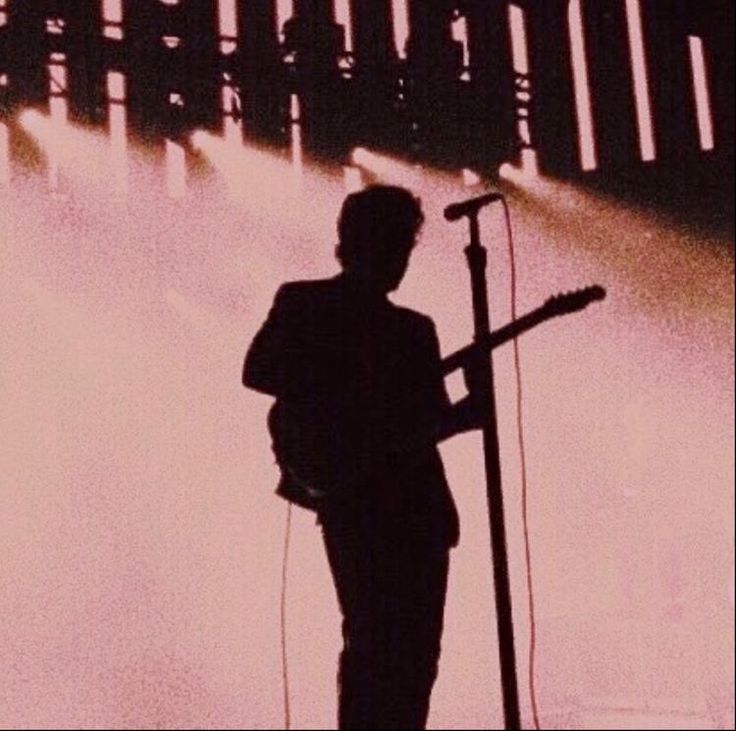 a man with a guitar standing in front of a microphone and some lights behind him