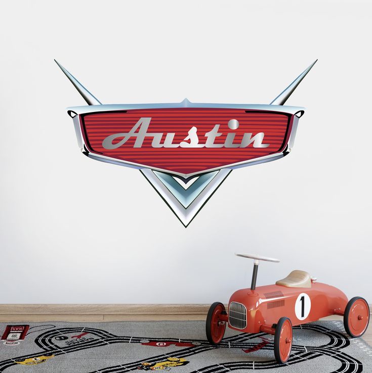 a red toy car sitting on top of a rug next to a wall mounted sign