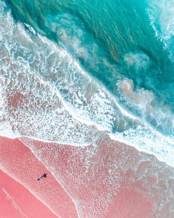 an aerial view of the ocean and beach with pink sand, blue water and waves