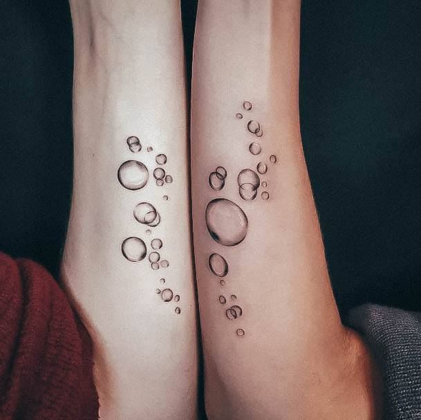 two people with matching tattoos on their feet, both have water drops coming out of them