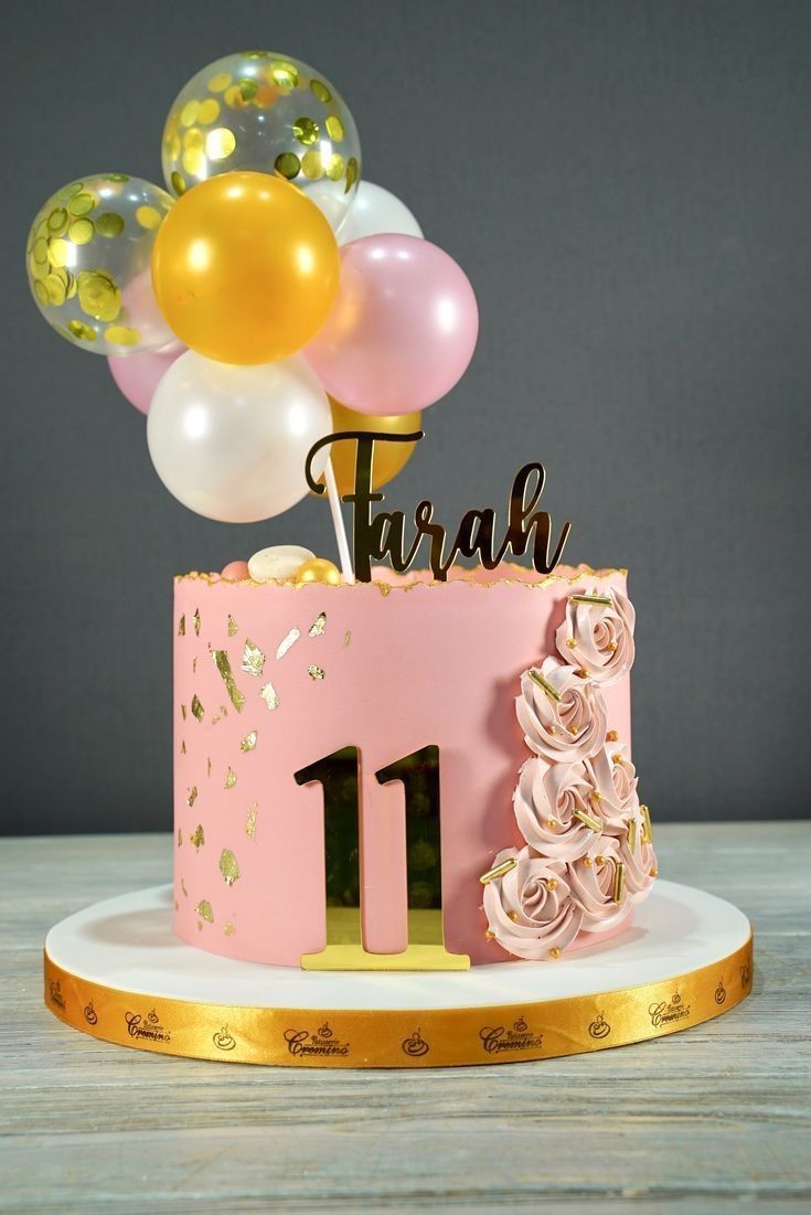 a pink and gold birthday cake with balloons in the shape of a number one on top