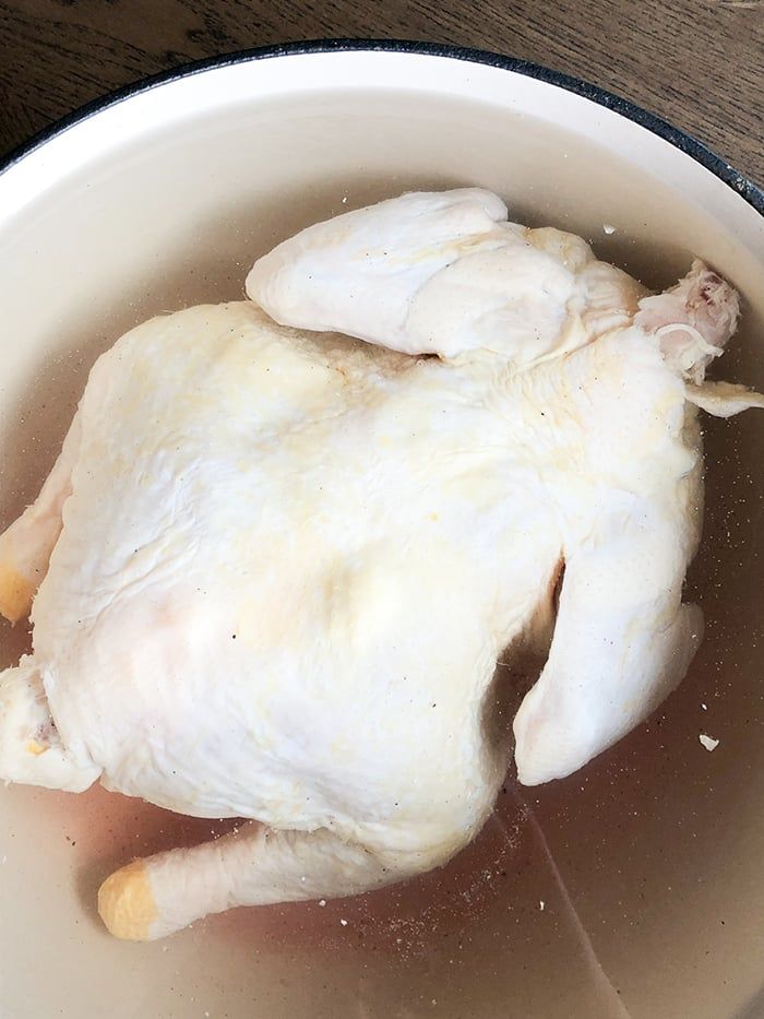 a cooked chicken in a white bowl on a wooden table