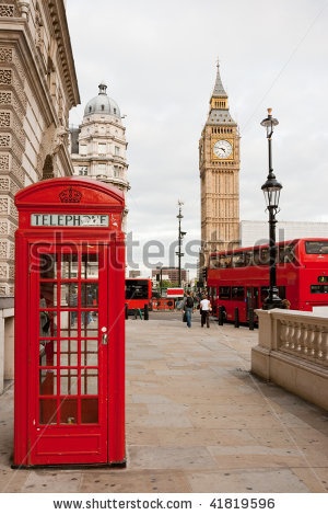 a red phone booth sitting on the side of a road next to a tall clock tower