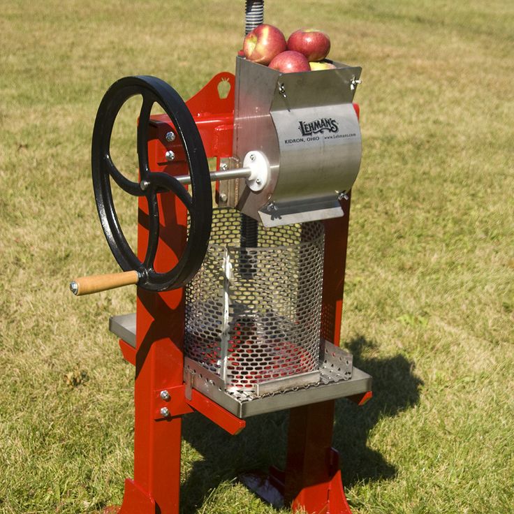 an apple cider sitting in the grass with apples on it's stand and wheel