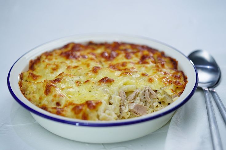 a white bowl filled with macaroni and cheese next to two silver spoons