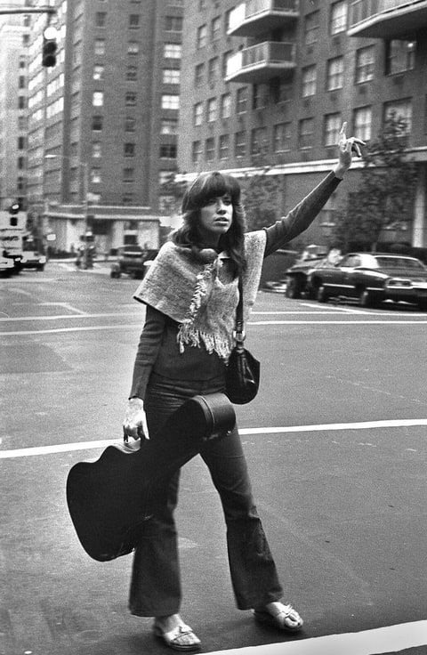 a woman is crossing the street with her hand in the air while holding two suitcases