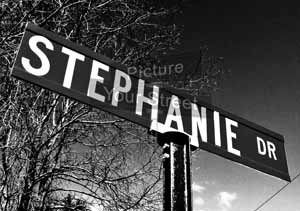 black and white photograph of the street sign for stephanie dr in front of some trees