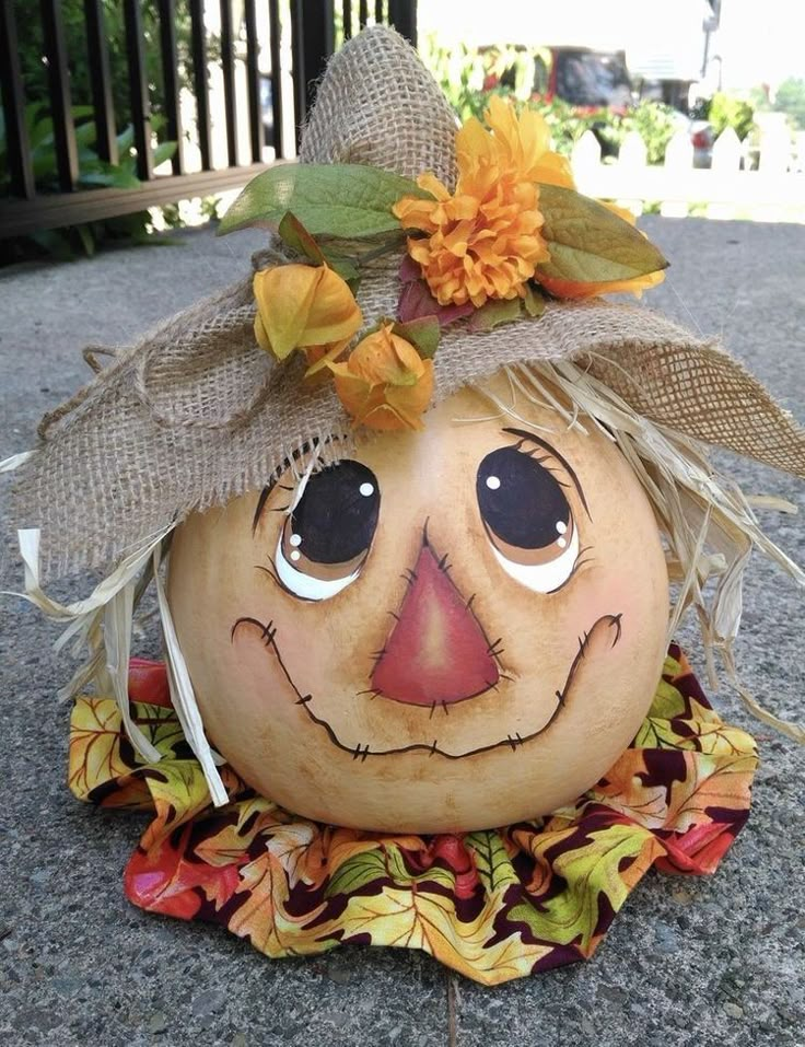 a pumpkin with a scarecrow's hat and leaves on it sitting on the ground