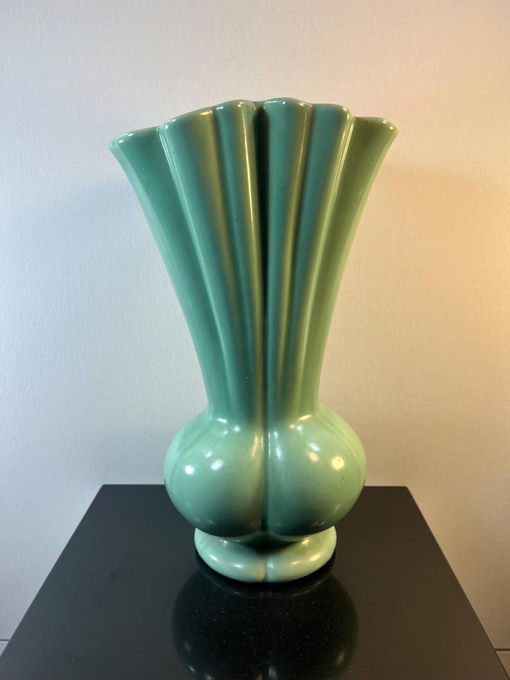 a green vase sitting on top of a black table next to a white wall and floor