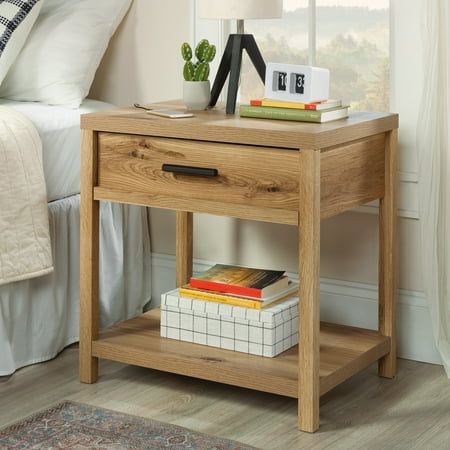 a nightstand table with books on it next to a bed