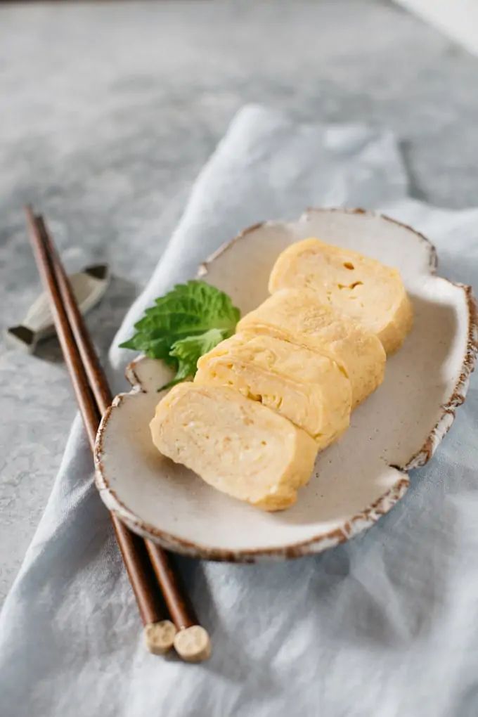 two chopsticks on a plate with some food in the bowl next to it