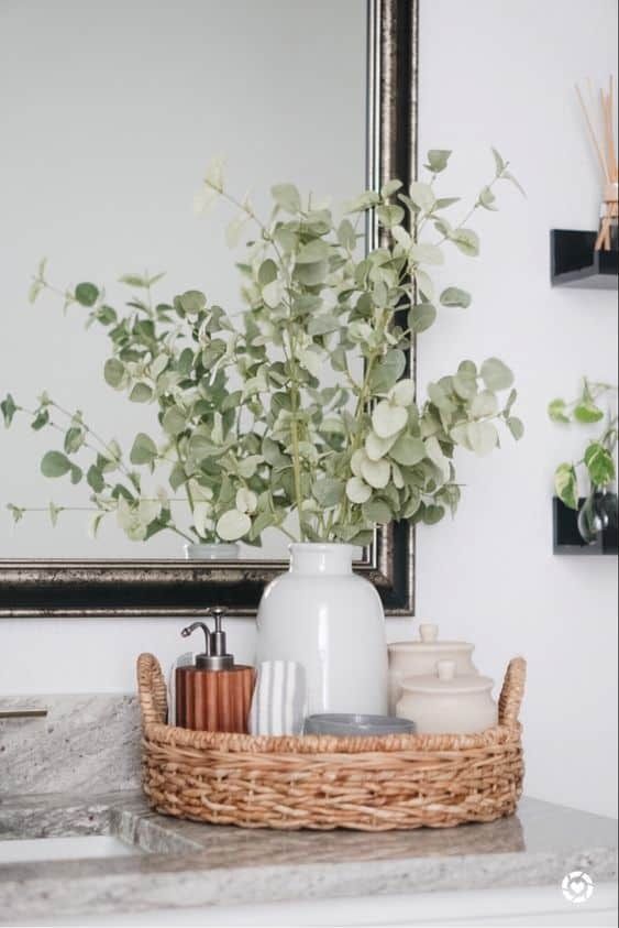 a white vase filled with flowers sitting on top of a bathroom counter next to a mirror