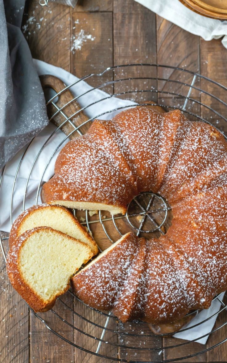 a pound cake on a cooling rack with slices cut from it and powdered sugar sprinkled on top