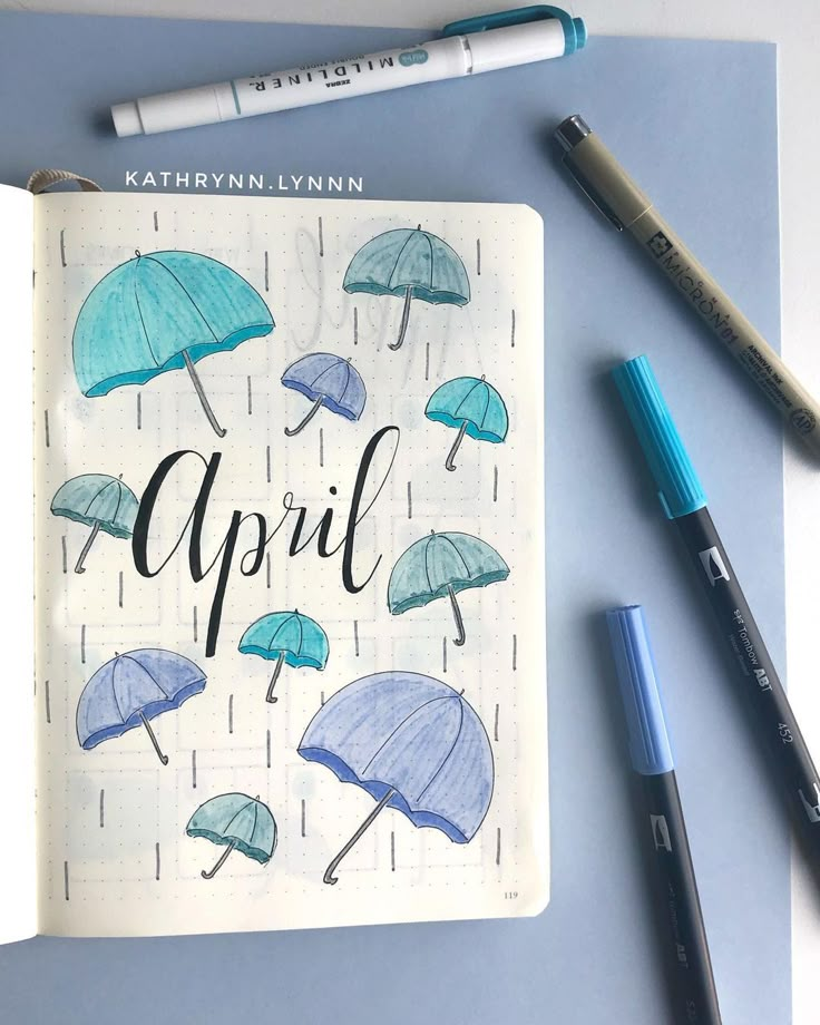 an open notebook with umbrellas drawn on it next to markers and pencils,