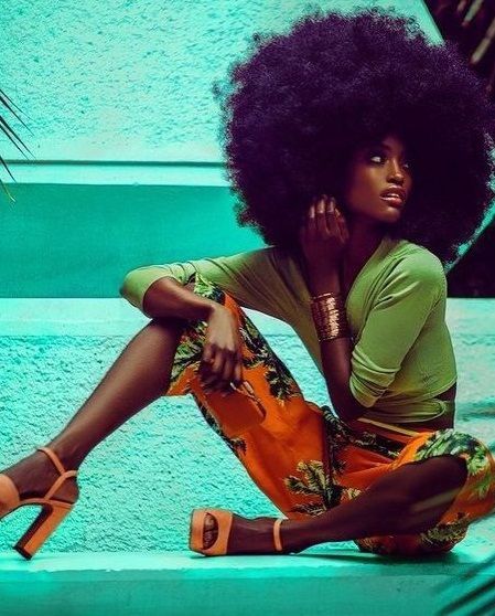 a woman with an afro sitting on the ground in front of palm trees and wearing high heels