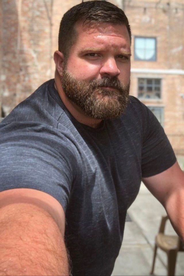 a man with a goatee and beard sitting at an outdoor table looking off into the distance