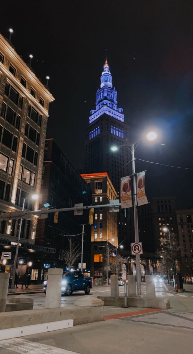 the tall building is lit up with blue lights in the city at night, along with other buildings