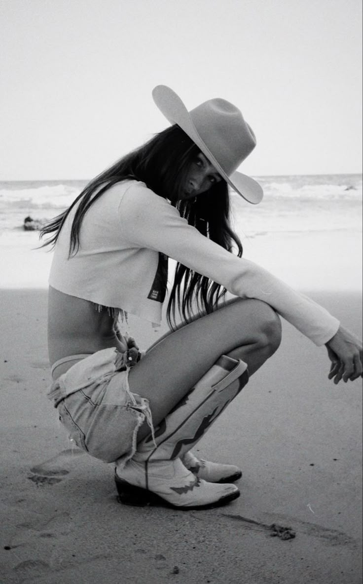 black and white photograph of a woman in cowboy hat kneeling on the sand at the beach