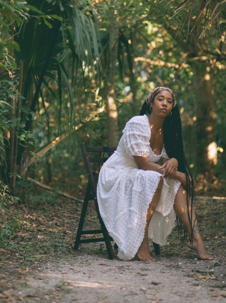 a woman is sitting on a chair in the middle of some trees and dirt road