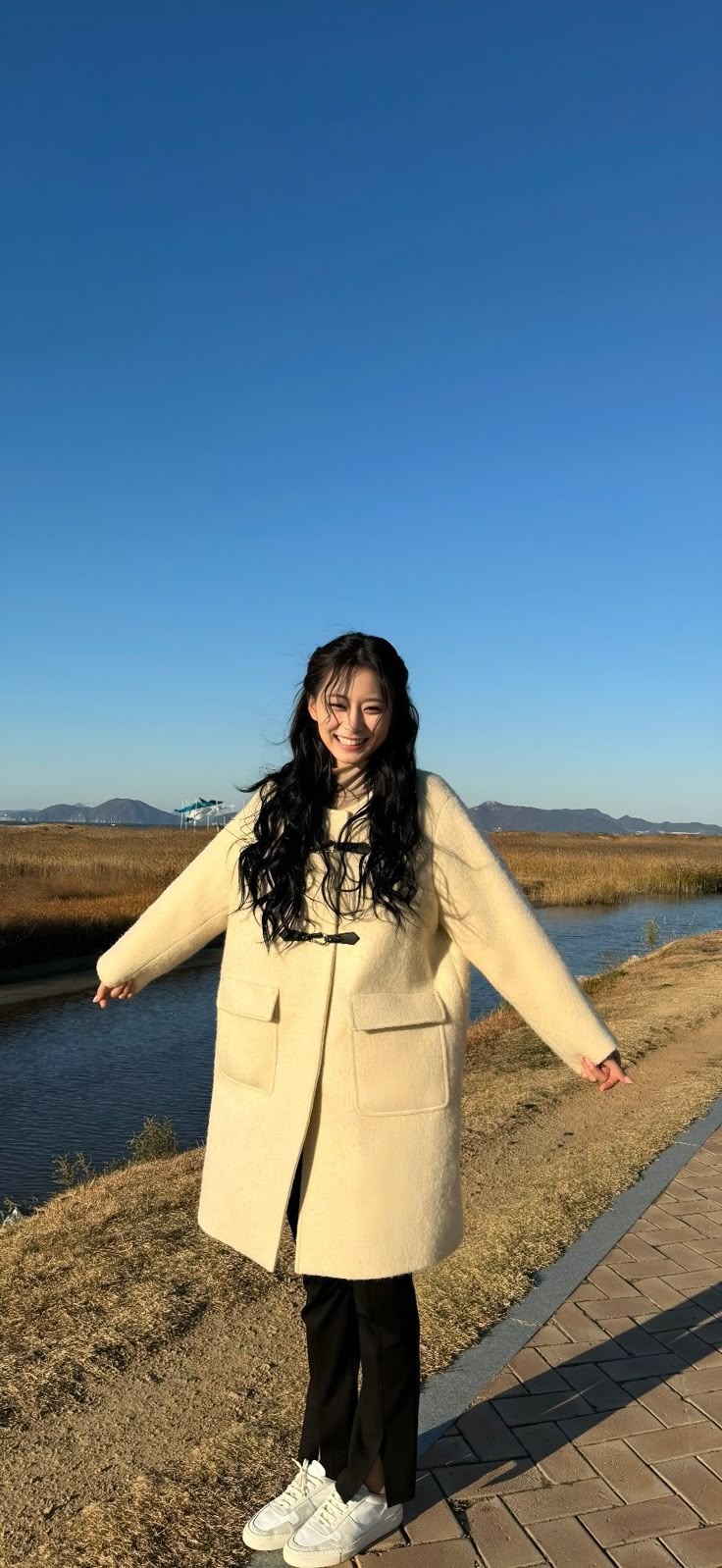 a woman standing on a sidewalk next to a body of water with her arms outstretched