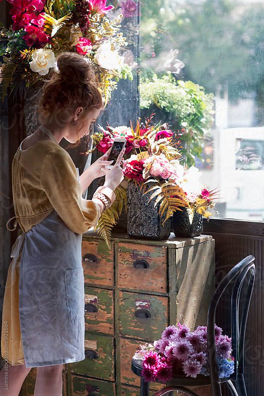 a woman standing in front of a window next to a dresser with flowers on it