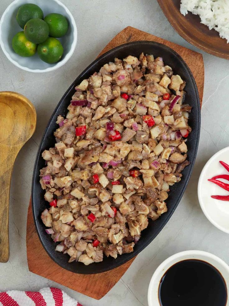 a pan filled with food sitting on top of a wooden cutting board next to bowls and spoons