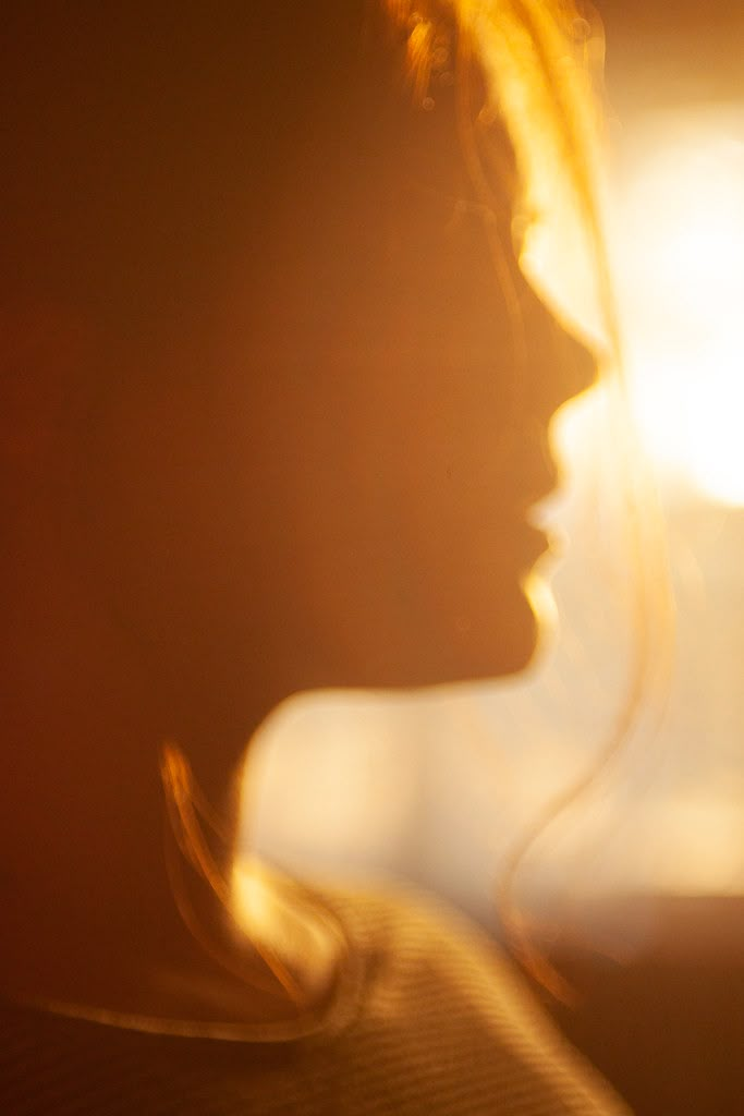 a blurry photo of a woman's face with the sun shining behind her