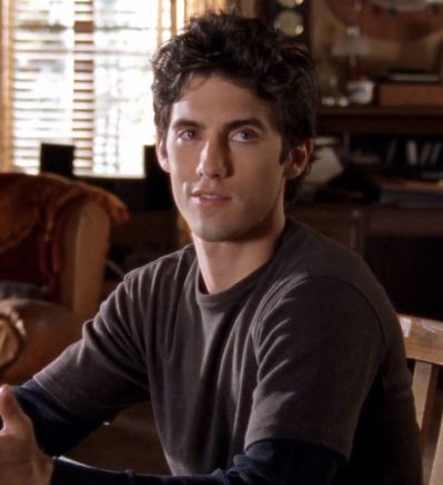 a young man sitting at a table in front of a window with the blinds open