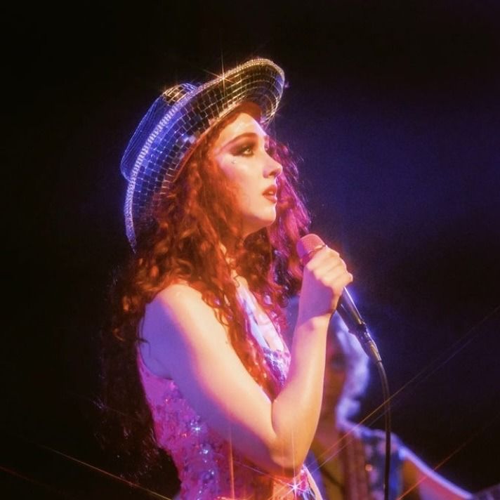 a woman with long red hair wearing a hat and holding a microphone in her hand