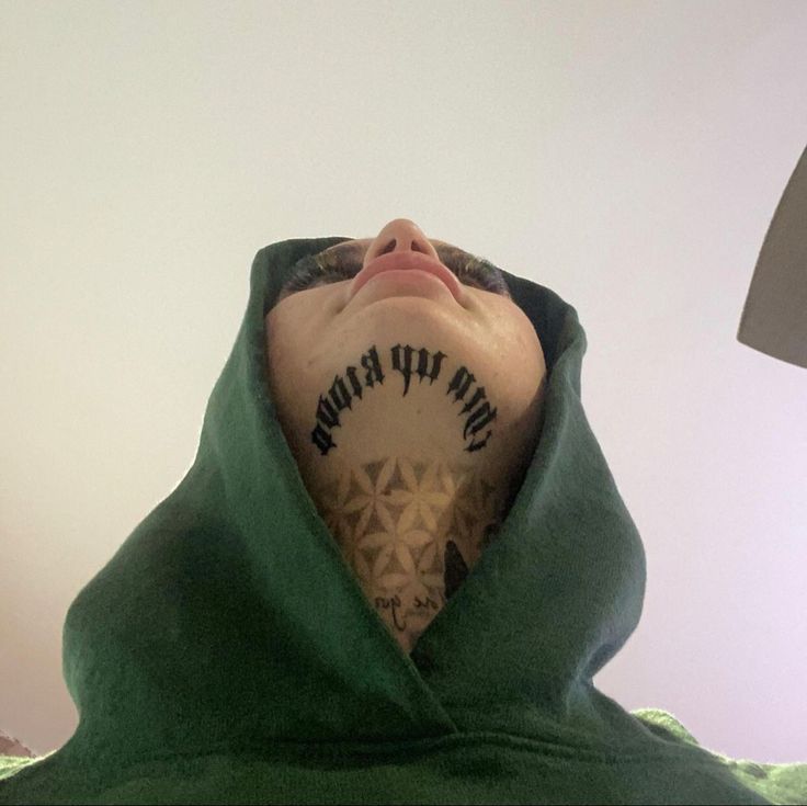 a man with tattoos on his neck and back covered in a green hoodie looking up into the sky