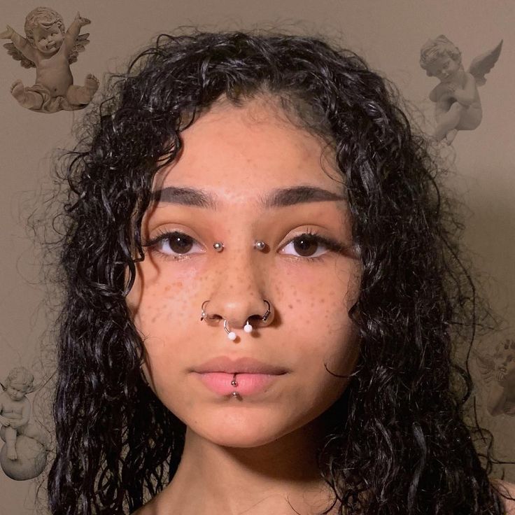 a young woman with freckles on her nose and nose piercings is looking at the camera