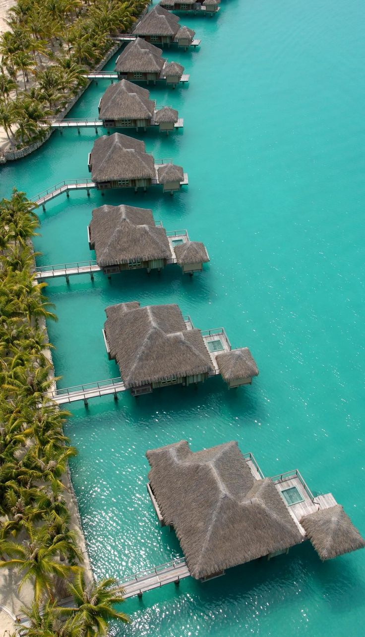 the water is crystal blue and clear with some huts on stilts in the middle