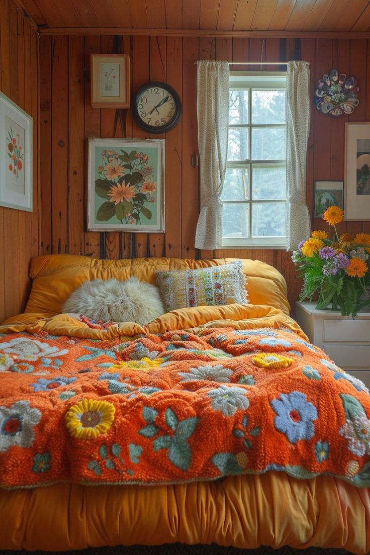 a bed with an orange bedspread covered in flowers and blankets next to a window